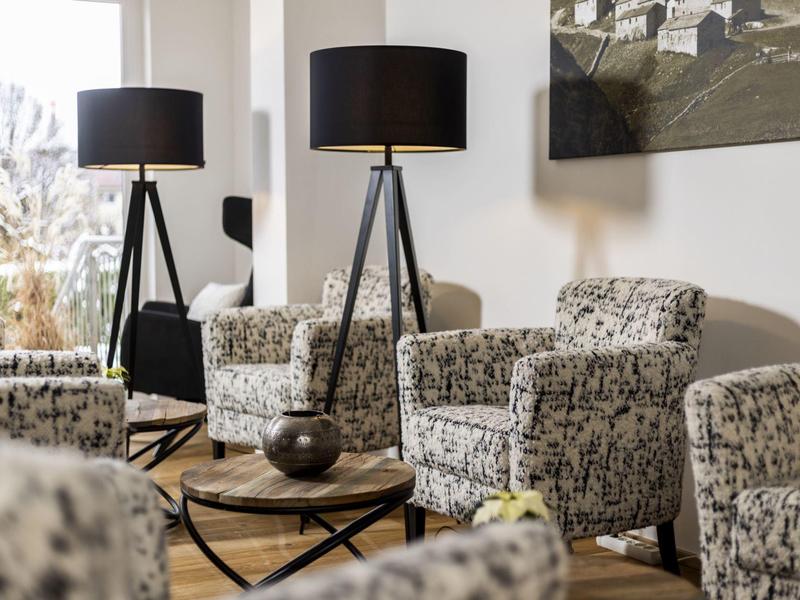 Accogliente zona d'attesa con poltrone a motivo e lampade da terra nere.