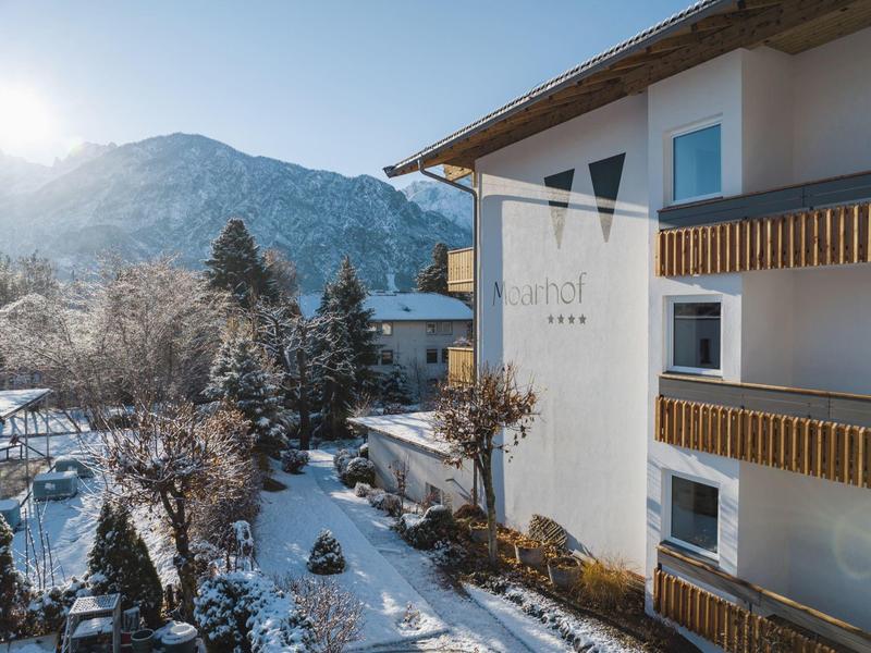 Hotel con balconi in legno sotto un cielo soleggiato e sfondo montano