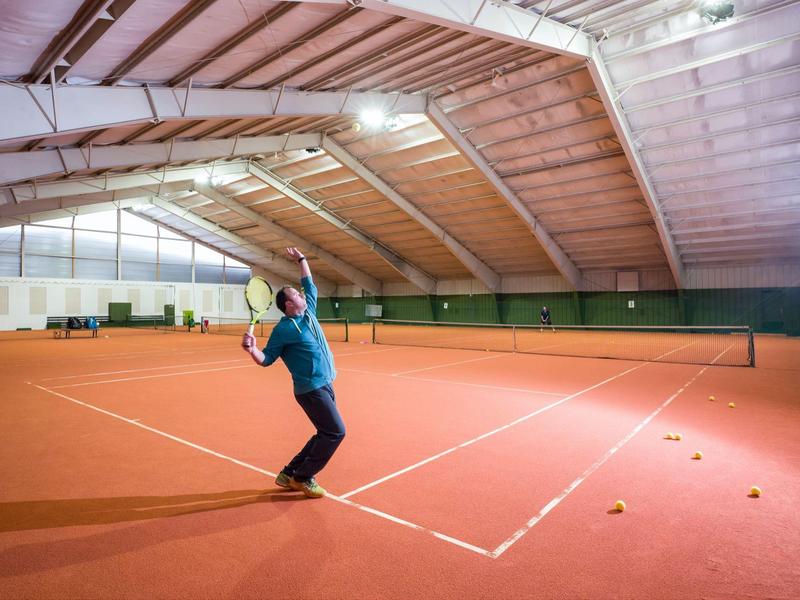 Ein Mann bereitet sich in einer großen Tennissporthalle auf einen Aufschlag vor.