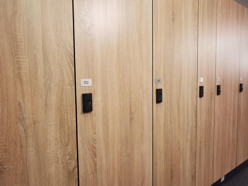 Eine lange Reihe von hellbraunen Holzspinden mit schwarzen Schlössern in einem Flur.