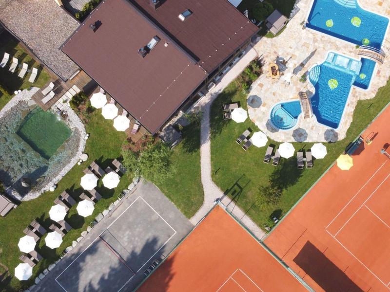 Überblick über Tennisplätze, Pools und Sonnenschirme mit Grünflächen und Wegen aus der Vogelperspektive.