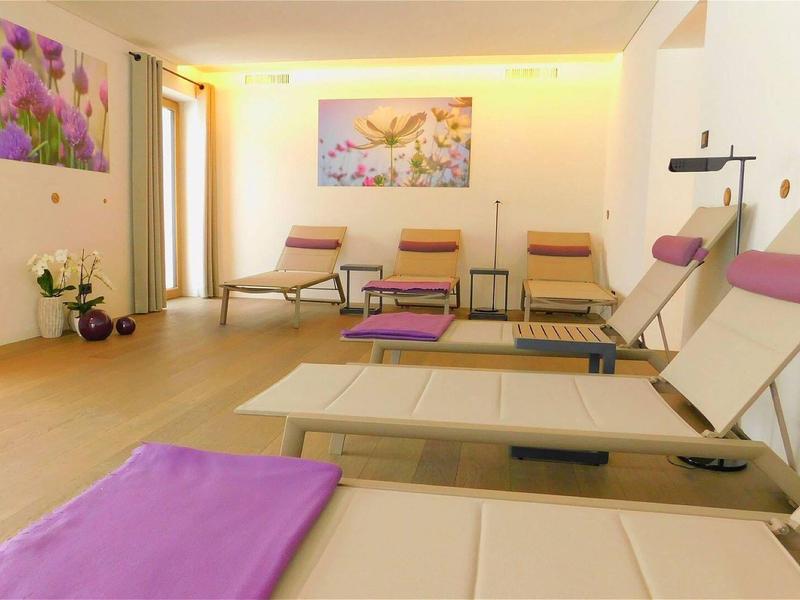 Heller Ruheraum mit Liegen und Stühlen, Wandbildern und sanfter Beleuchtung, in warmen Farben.