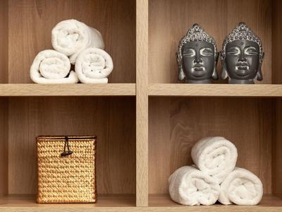 Holzregal mit gefalteten weißen Handtüchern, zwei Buddha-Köpfen und einem geflochtenen Korb.