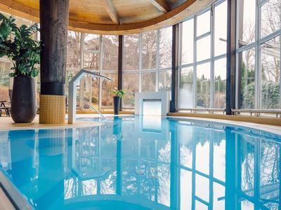 Innenbereich-Schwimmbad mit großen Fenstern, blauem Wasser und Pflanzen neben Säulen.