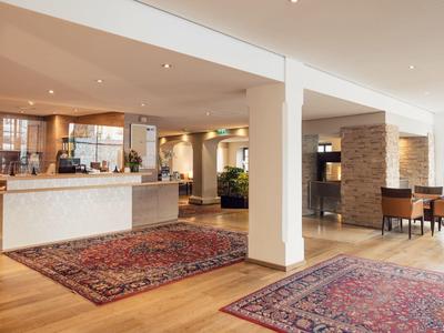 Großer Empfangsbereich mit Holzfußboden, Teppichen und einem hellen Empfangstresen.