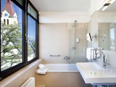 Moderní koupelna s velkou vanou, okenní stěnou a umyvadlem.