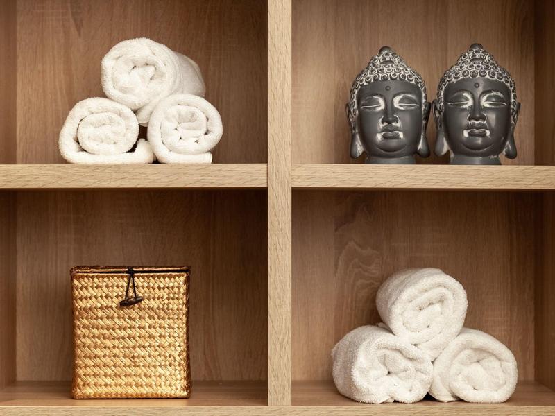 Holzregal mit gefalteten weißen Handtüchern, zwei Buddha-Köpfen und einem geflochtenen Korb.