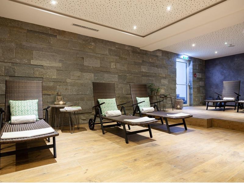 Moderner Ruheraum mit Liegestühlen, Holzboden, Steinterrassenwand und gedämpftem Deckenlicht.