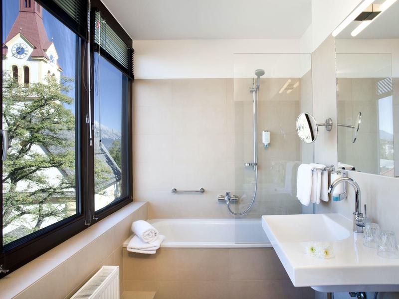 Helles Badezimmer mit großer Fensterfront, Badewanne, Waschbecken und weißen Handtüchern.