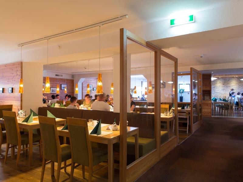 Großes, helles Restaurant mit Holztrennwänden, grünen Stühlen und gedeckten Tischen.