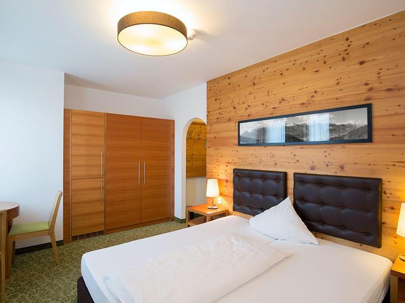 Hell eingerichtetes Schlafzimmer mit Doppelbett, Holzwand, Kleiderschrank und zwei Nachttischlampen.