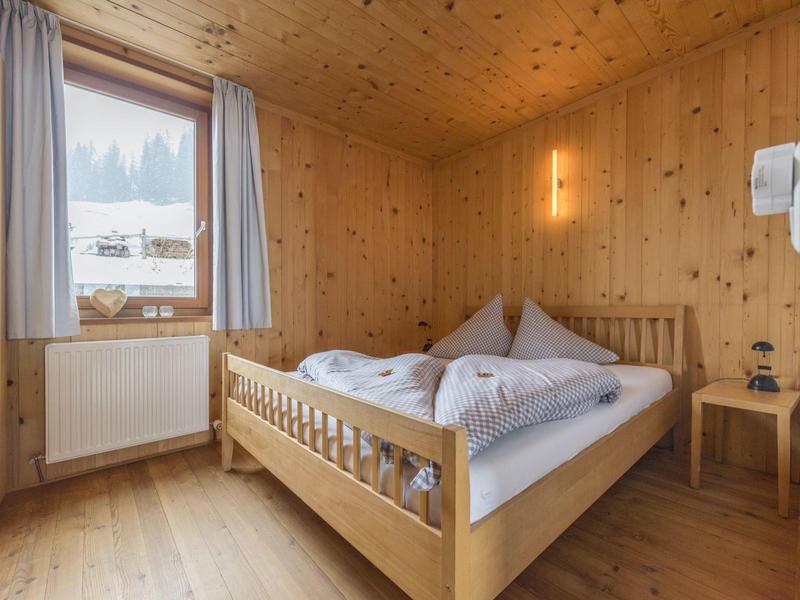 Gemütliches kleines Schlafzimmer mit Holzwänden, Holzboden, Doppelbett und Fenster mit Blick ins Freie.