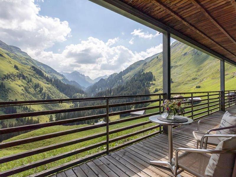 Balkon mit Stühlen und Tisch, Blick auf grüne Berge unter bewölktem Himmel.
