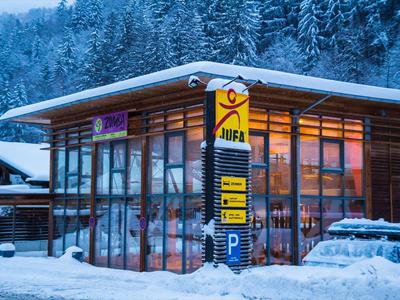 Modernes Gebäude mit großen Glasfenstern, Schnee und Wald im Hintergrund bei Dämmerung.