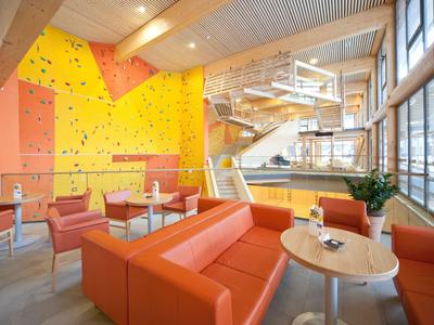 Espace lounge moderne avec canapés orange et mur d'escalade dans un espace lumineux avec beaucoup de lumière naturelle.