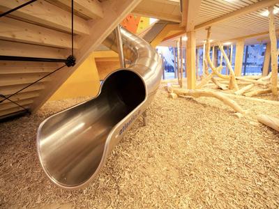 Stainless steel slide in a play area with wooden flooring and wood framework.