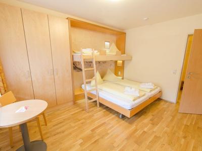 Brightly furnished hotel room with bunk bed, table, chair, and large wardrobe.