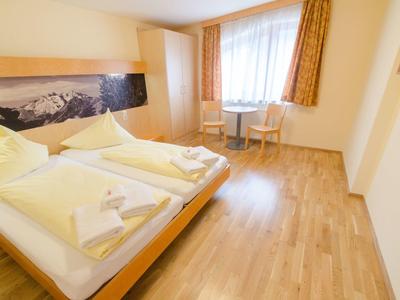 Bright hotel room with double bed, wooden floor, two chairs, and window with curtains.