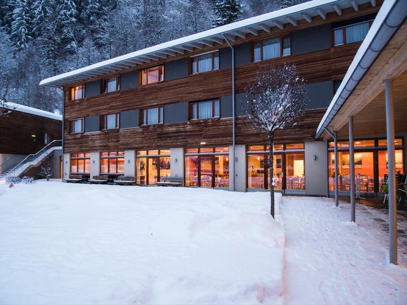 Modern hotel building with large windows and snowy courtyard in the evening.