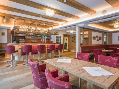 Bar d'hôtel accueillante avec comptoir en bois, tabourets rouges et tables avec chaises rouges.