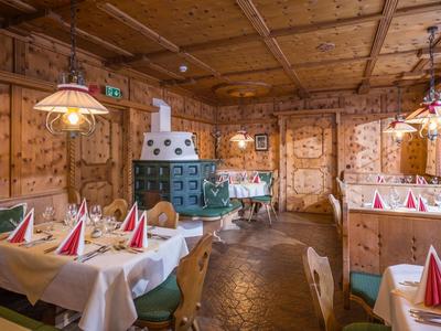 Restaurant rustique avec lambris en bois, poêle en carrelage vert et tables dressées avec des serviettes rouges.