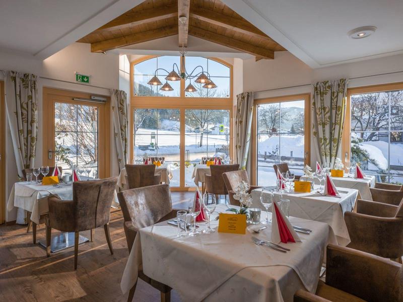 Salle de petit-déjeuner chaleureuse avec tables dressées et vue sur paysage enneigé à travers grandes fenêtres.