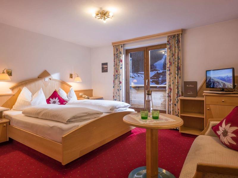 Chambre d'hôtel confortable avec lit double, tapis rouge, meubles en bois et vue sur un paysage enneigé.