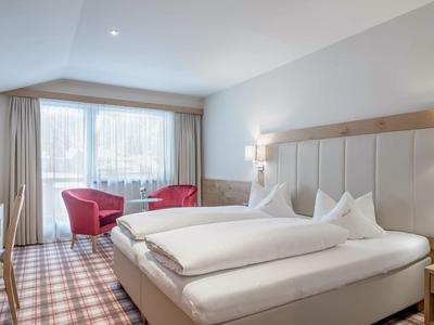 Modern hotel room with large bed, armchairs, and window with curtains