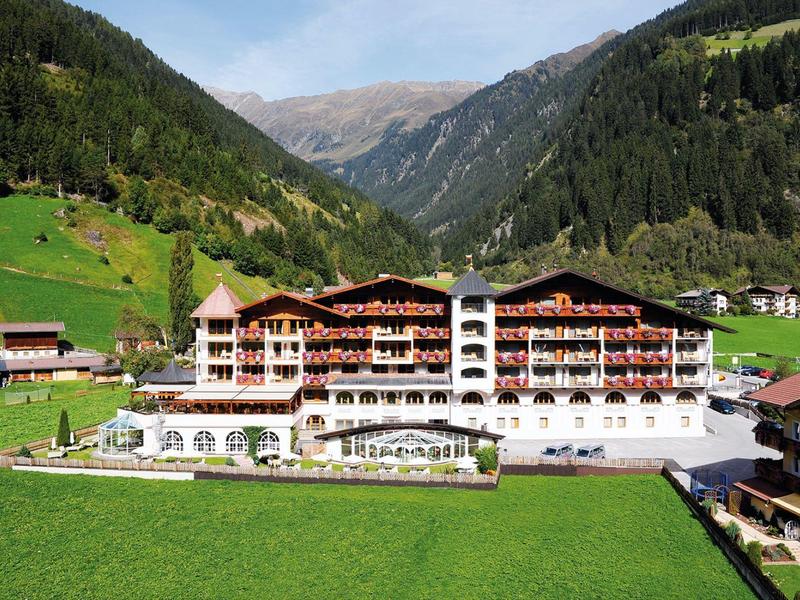 Large hotel building in a green mountain valley with forested slopes in the background.