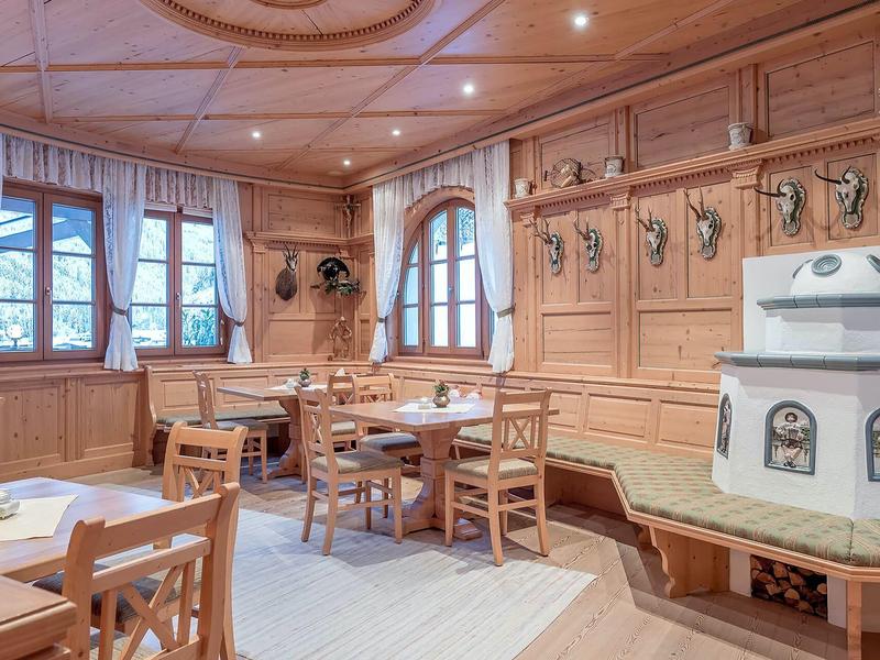 Traditional wooden dining room with tables, chairs, and a white tiled stove.