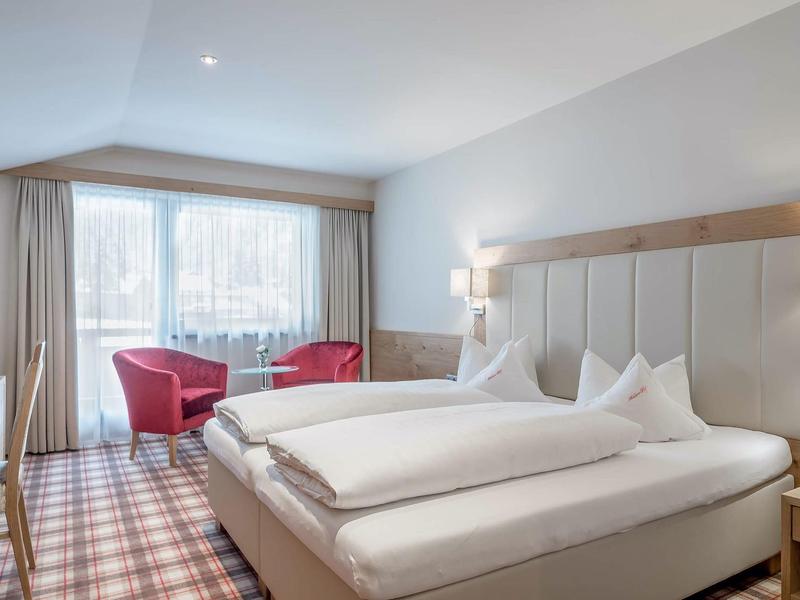 Modern hotel room with large bed, armchairs, and window with curtains