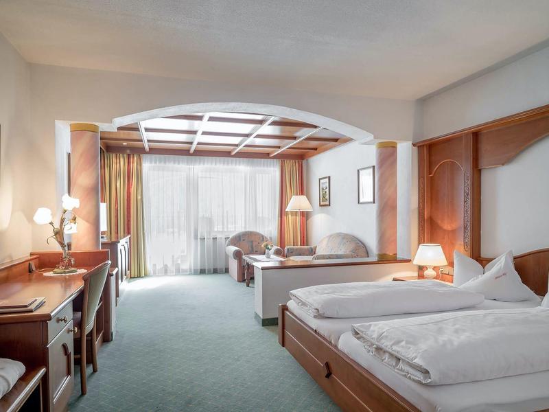 Spacious hotel room with two beds, desk, and window with curtains.