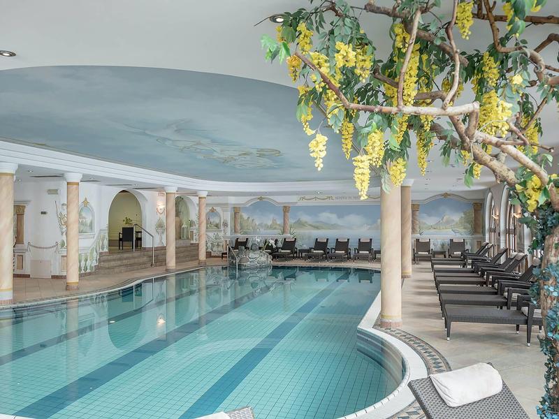 A luxurious indoor pool with lounge chairs and a decorative ceiling painted like the sky.