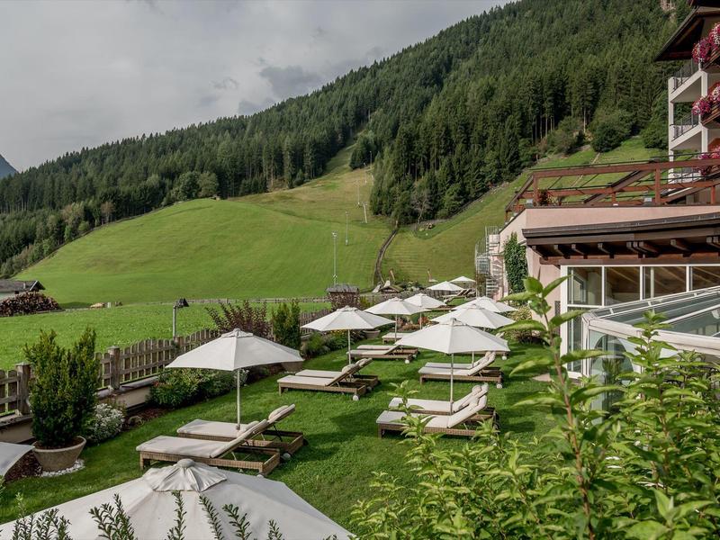 Green hillside with lounge chairs and umbrellas in front of a mountain hotel building.