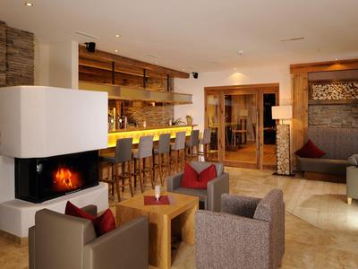 Area lounge moderna con camino, poltrone e sgabelli da bar in luce calda.