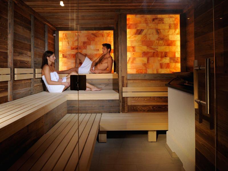 Atmosfera rilassante in una sauna di legno con due persone e pannelli murali in pietra di sale illuminati.