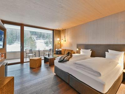 Modern hotel room with double bed, wooden ceiling, and large windows with mountain view.