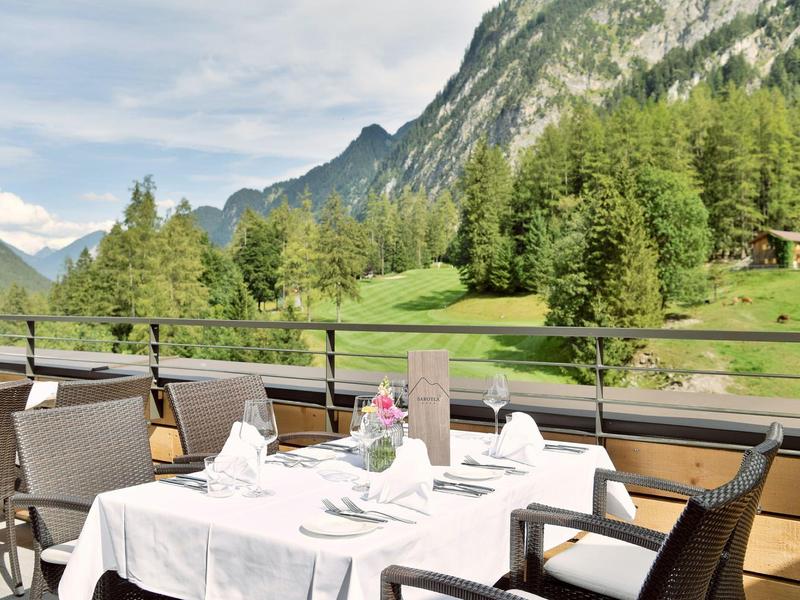 Terrace with set tables, chairs, and mountain view under clear sky.