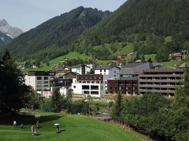 Mountain hotel with large lawn in front and forested hills in the background.