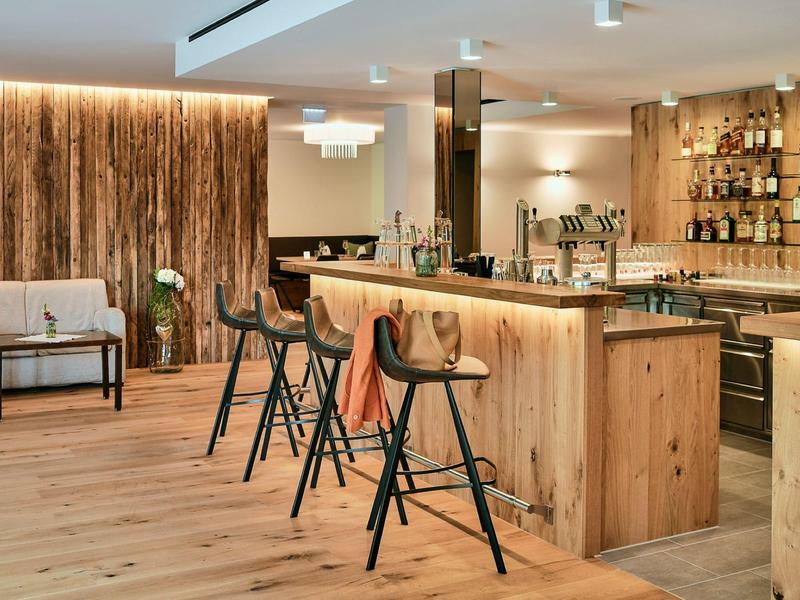 Modern hotel bar area with wooden elements, bar stools, and a relaxed seating area.