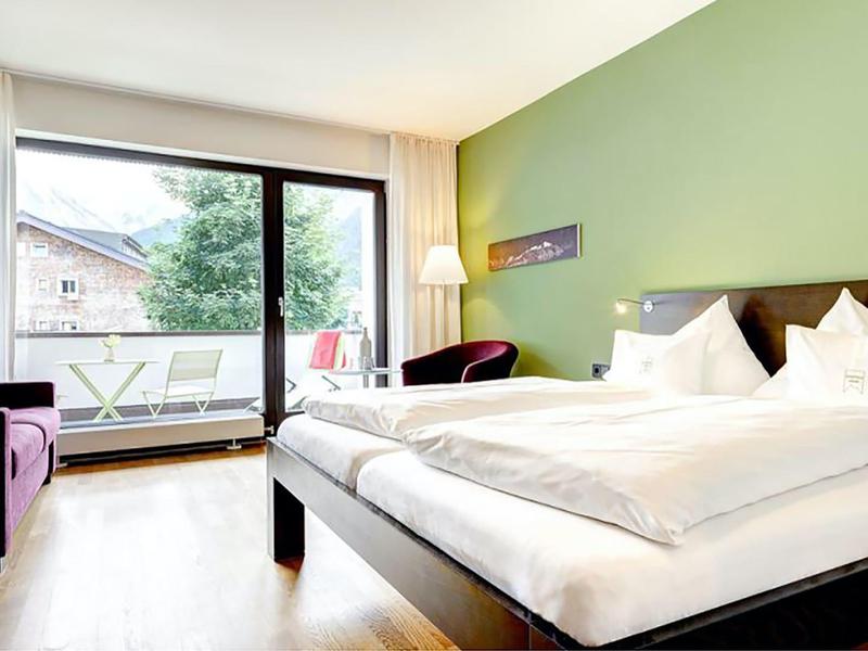 Bright hotel room with double bed, green painted wall, and balcony with seating area.