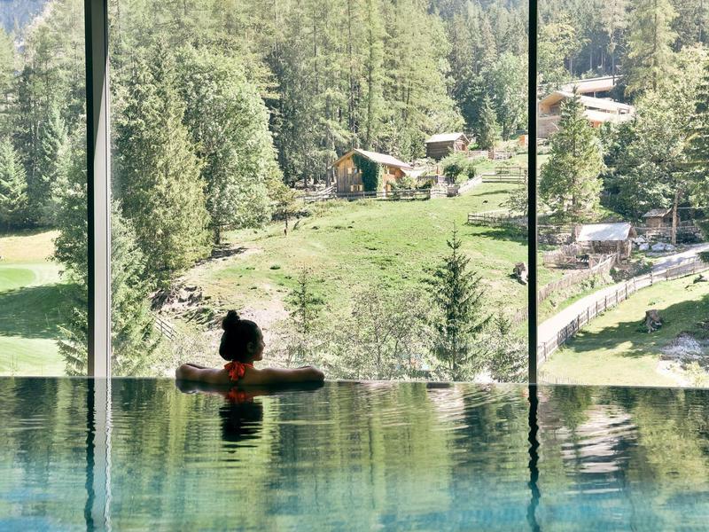 Person relaxing in indoor pool with panoramic view of wooded hills and nature