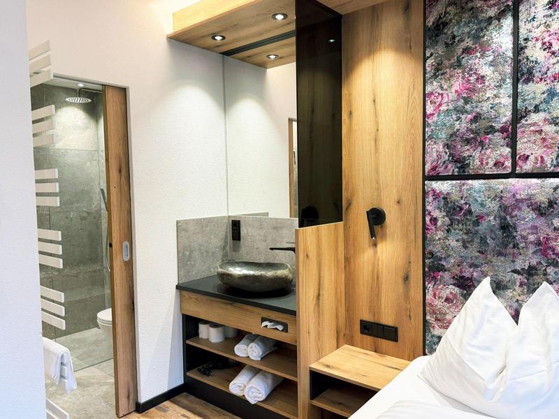 Chambre d'hôtel moderne avec étagères en bois, lavabo et panneau mural décoratif à côté du lit.