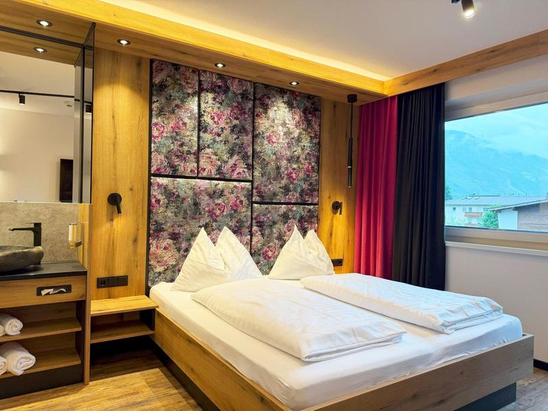 Chambre d'hôtel confortable avec lit double, décoration murale florale et fenêtre panoramique avec vue sur la montagne.