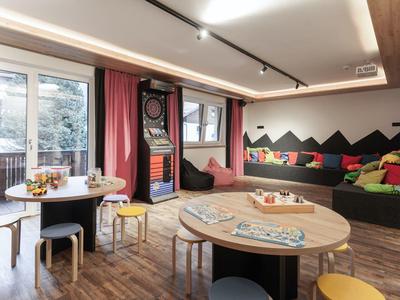 Gemütlicher Innenraum mit Sitzkissen, Rundtischen und einem Dartboard neben großen Fenstern.