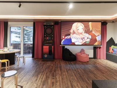 Moderner Gemeinschaftsraum mit Dartboard, Sitzsäcken und großem Bildschirm in einem Hotel.