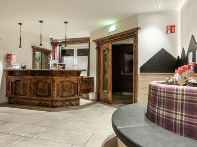 Hotelempfang mit rustikalem Holztresen, Sitzbereich mit kariertem Polster und dekorativen Bergmotiven.