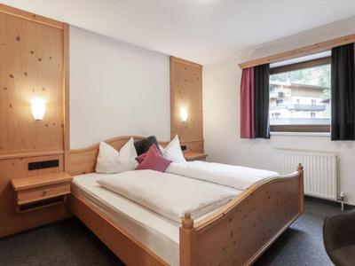 Helles Hotelzimmer mit Holzbettrahmen, zwei Einzelbetten, Nachttischlampe und Fenster mit Blick auf Gebäude.