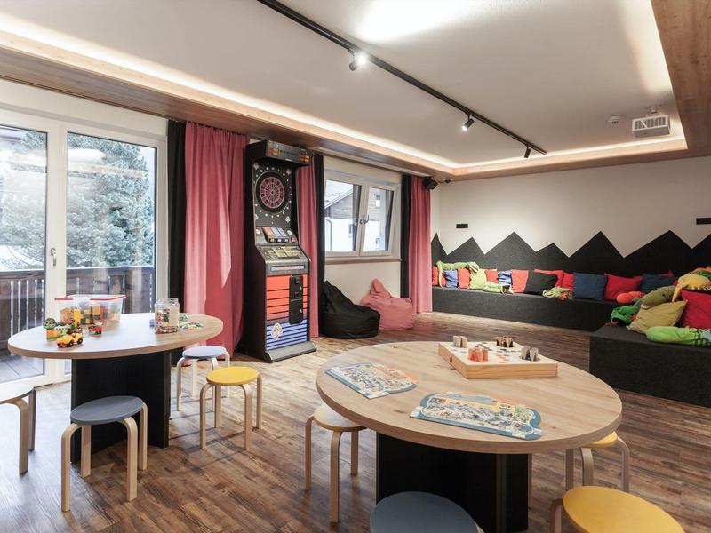 Gemütlicher Innenraum mit Sitzkissen, Rundtischen und einem Dartboard neben großen Fenstern.
