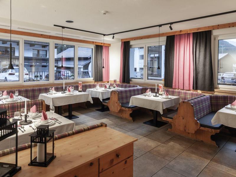 Gemütlicher Frühstücksraum mit Holzmöbeln und großen Fenstern mit Blick auf ein Dorf.